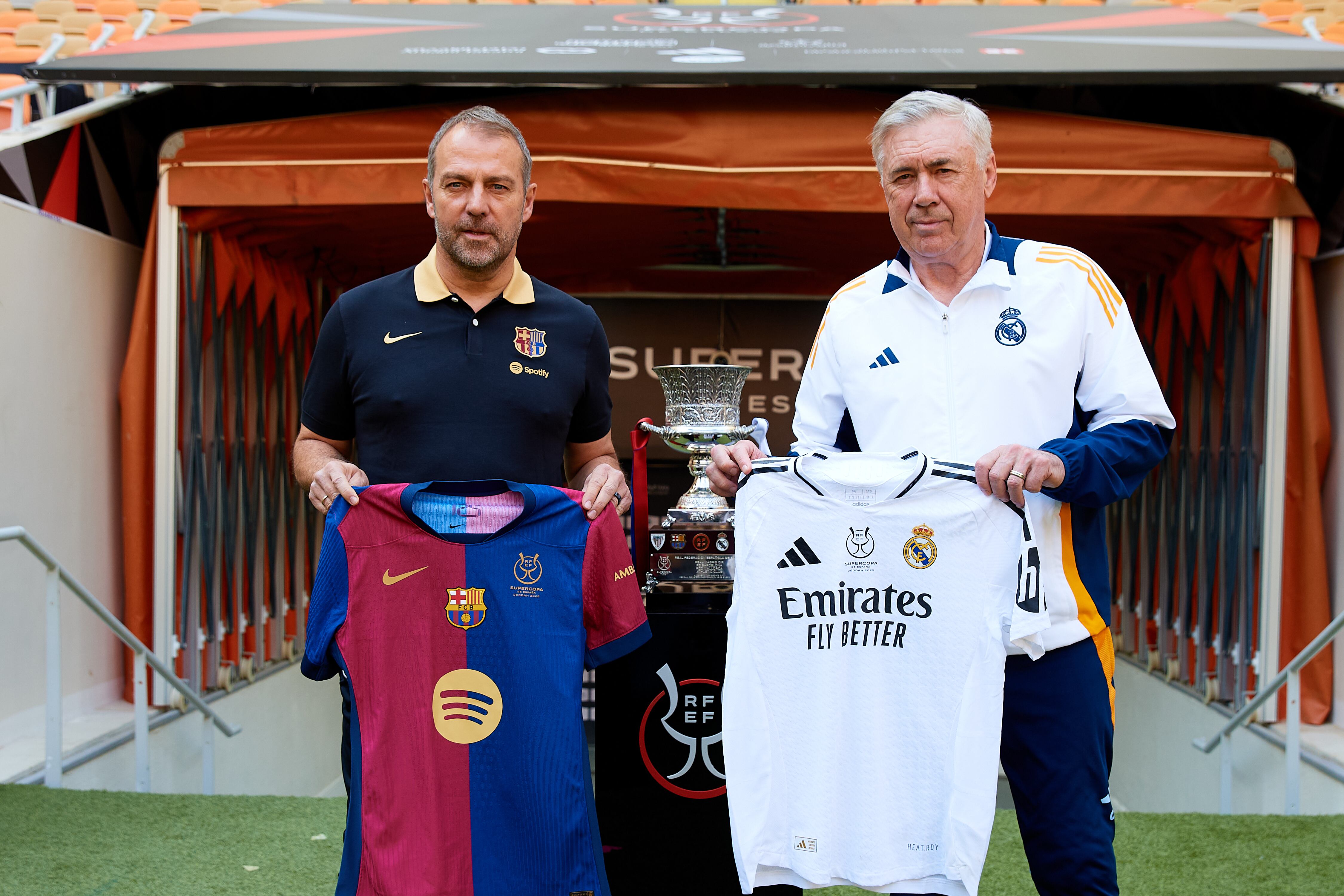 Hansi Flick y Carlo Ancelotti posan con casacas de sus equipos junto al trofeo