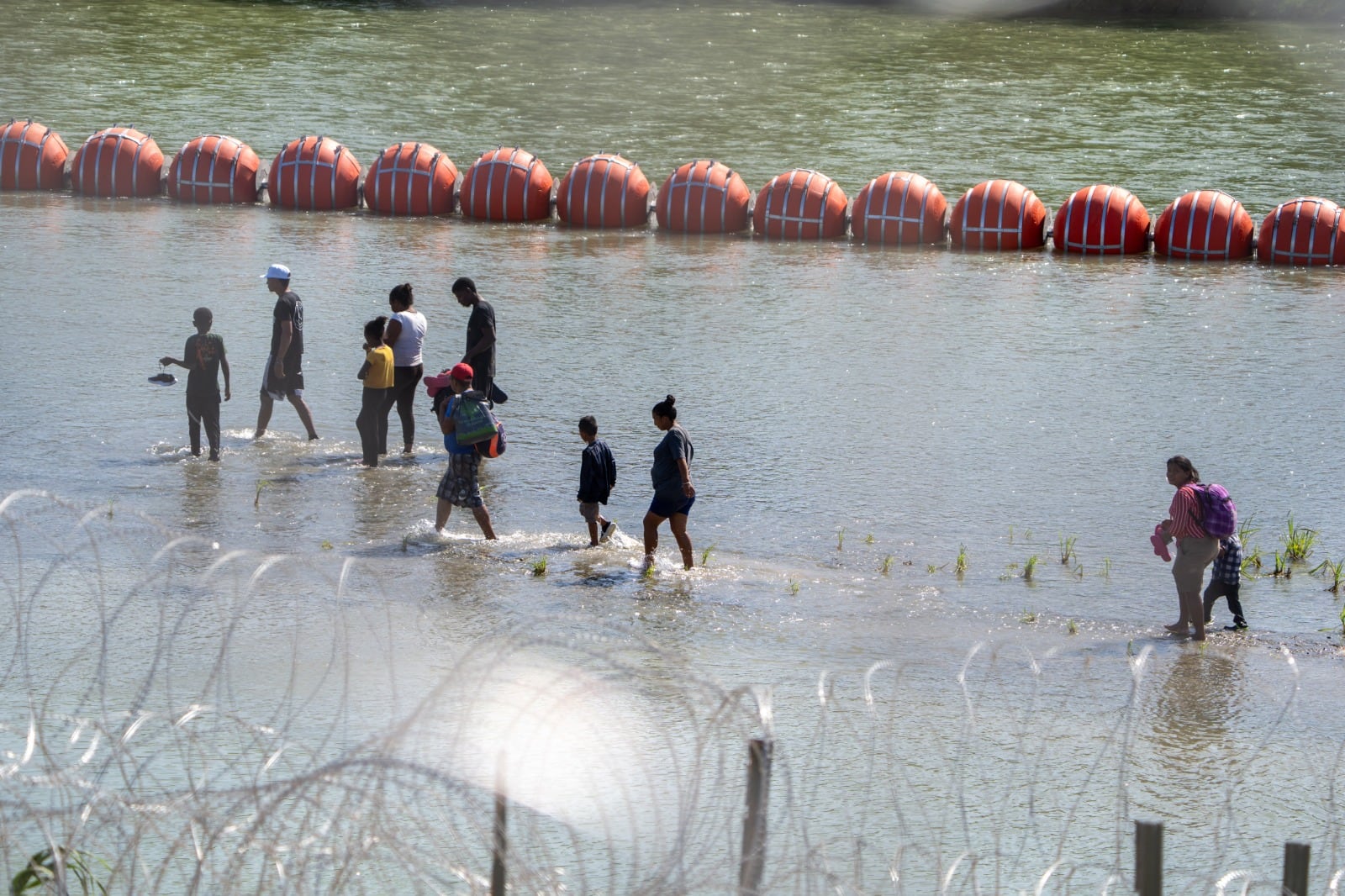 Migrantes caminan en la orilla del Río Grande frente a Eagle Pass, Texas.