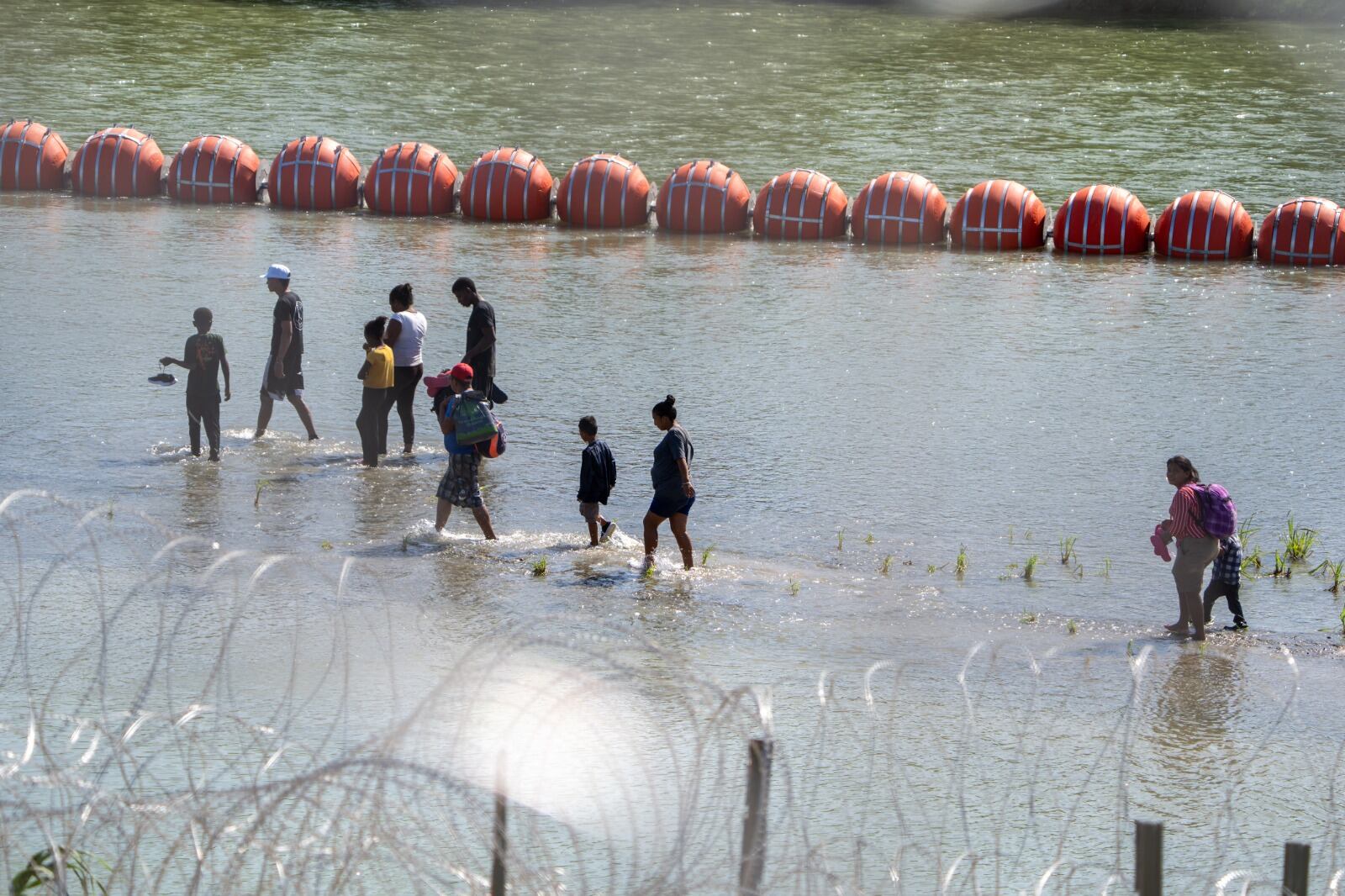 Migrantes caminan en la orilla del Río Grande frente a Eagle Pass, Texas.
