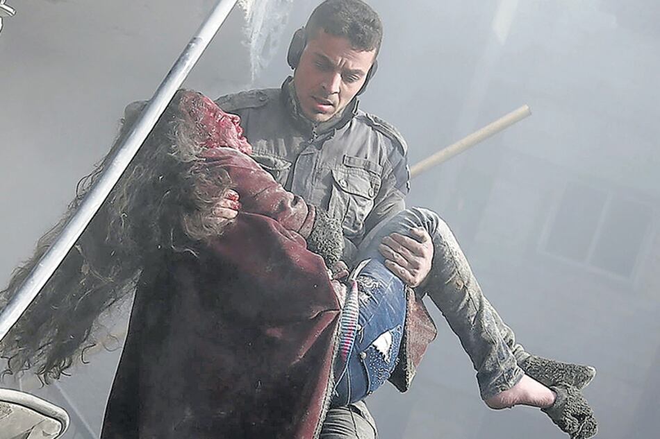 Un voluntario de la defensa civil levanta a una niña herida tras un bombardeo en Guta.