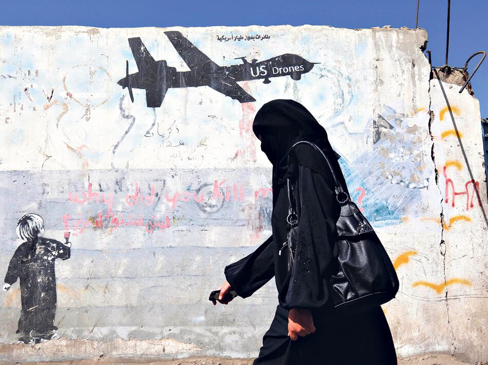 Una mujer yemení pasa al lado de un graffiti que condena las operaciones militares de EE.UU.