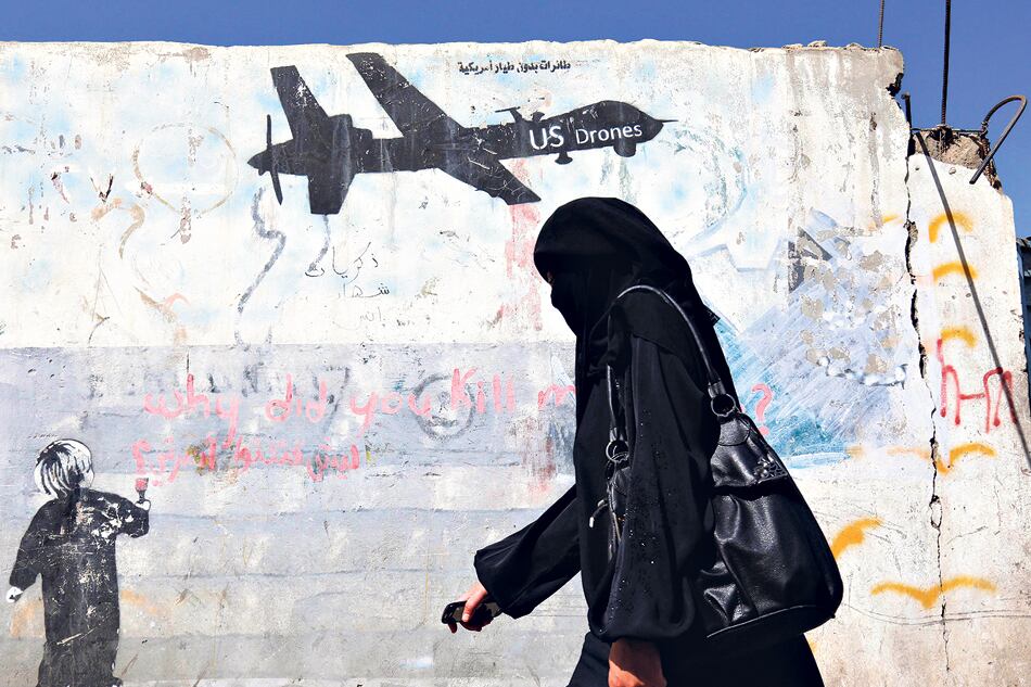 Una mujer yemení pasa al lado de un graffiti que condena las operaciones militares de EE.UU.