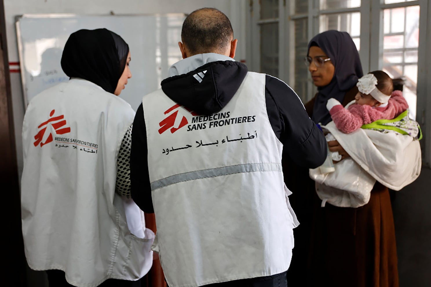 A Palestinian woman arrives with a child at the Doctors Without Borders or Medecins Sans Frontieres (MSF) clinic, in the al-Rimal neighborhood of Gaza City on new year's Eve, December 31, 2025. Israel has said 37 aid organisations will be banned from operating in Gaza from January 1, 2026, unless they comply with guidelines requiring detailed information on Palestinian staff, drawing criticism from the United Nations and the European Union. (Photo by Omar AL-QATTAA / AFP)