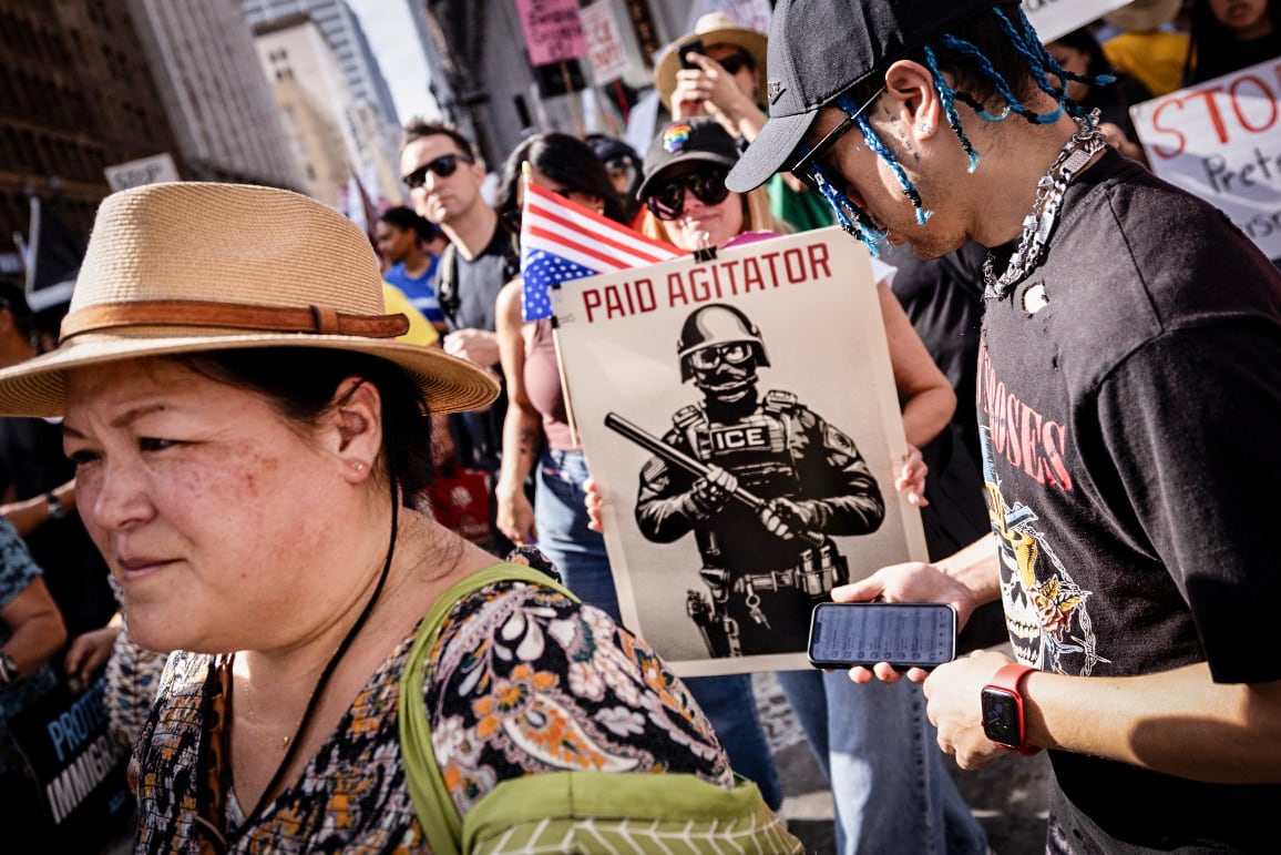Demonstrators hold a sign depicting an ICE agent as a paid agitator during the "No Kings" national day of protest in Los Angeles on March 28, 2026.