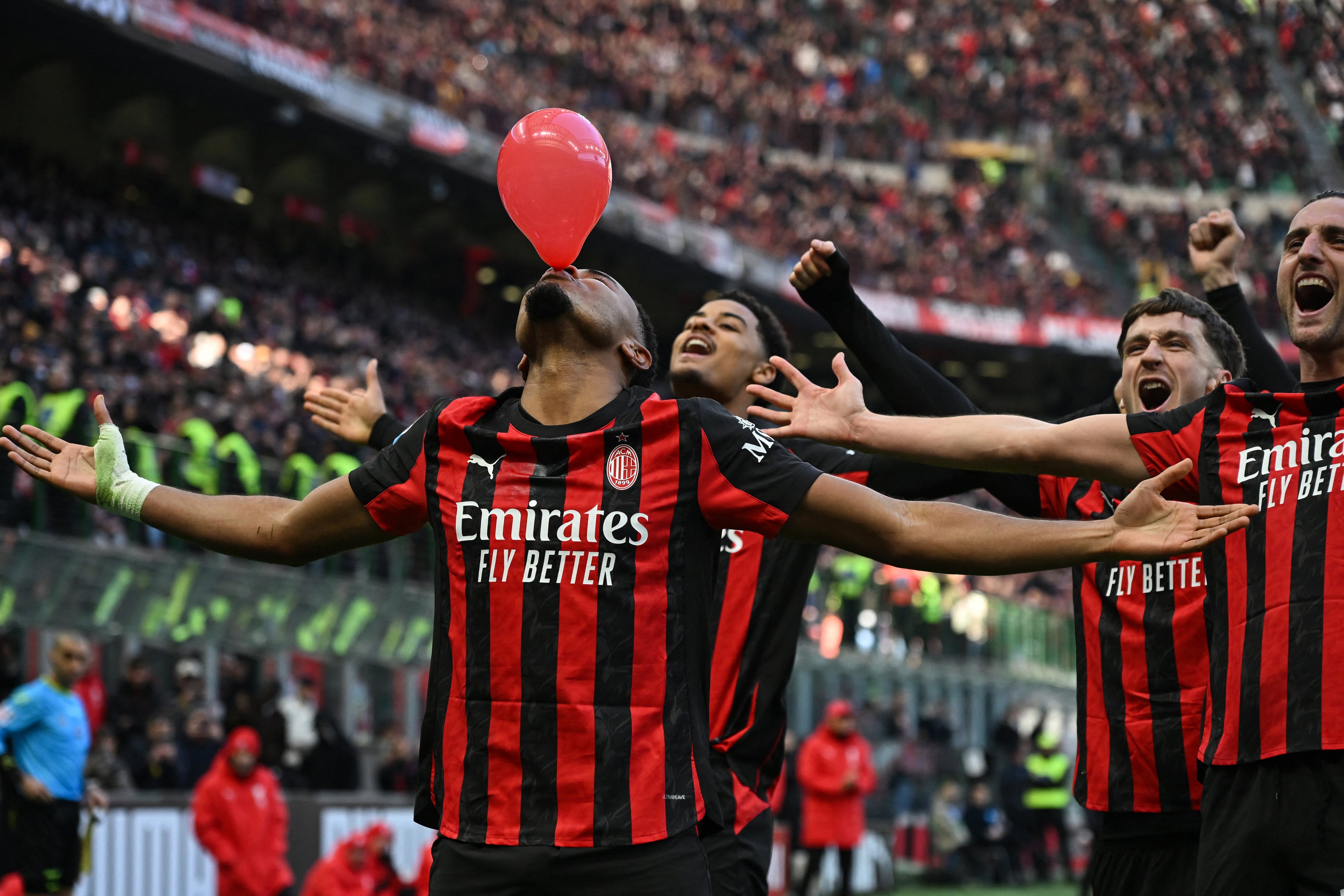 AC Milan's French forward #18 Christopher Nkunku (L) inflates a balloon as he celebrates after scoring his team second goal during the Italian Serie A football match between AC Milan and Hellas Verona at the San Siro stadium in Milan, northern Italy, on December 28, 2025. (Photo by Piero CRUCIATTI / AFP)