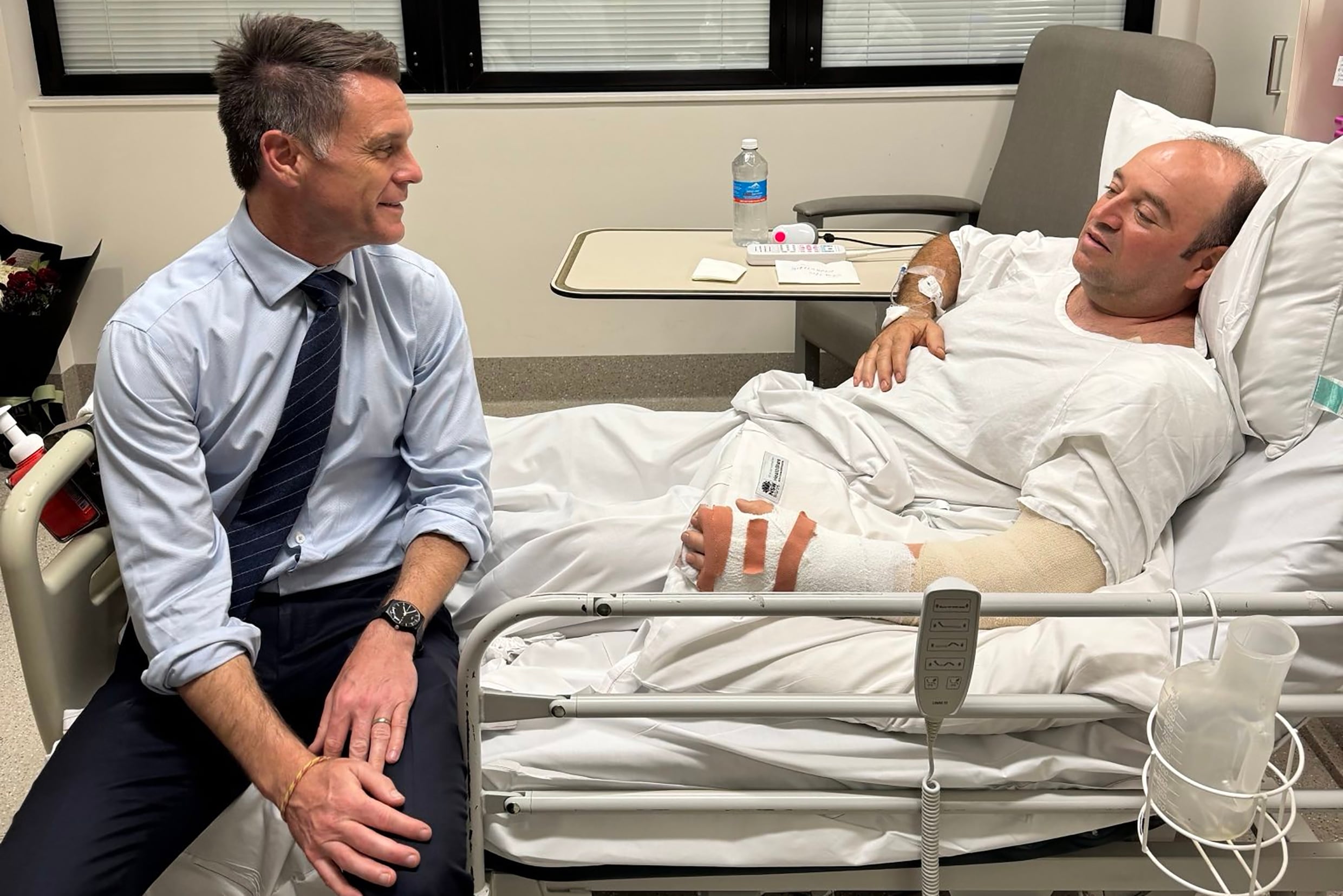 SÍDNEY, 15/12/2025.- Fotografía publicada en el perfil de X del líder político de Nueva Gales del Sur, Chris Minns, que muestra a Minns (i) visitando en el hospital a Ahmed al Ahmed, el hombre que desarmó a uno de los autores del atentado perpetrado ayer en Sídney. Junto a la fotografía, Minns define a Ahmed como "un héroe de verdad" cuya "increíble valentía sin duda salvó innumerables vidas al desarmar a un terrorista con un enorme riesgo personal". Ahmed, de 43 años, se escondió el domingo detrás de unos vehículos para sorprender a uno de los asaltantes y forcejear con él hasta quitarle con sus propias manos el rifle con el que disparaba a los transeúntes en la popular playa de Bondi. Como consecuencia, Ahmed recibió disparos en el brazo y la mano. EFE/ Chris Minns vía red social X