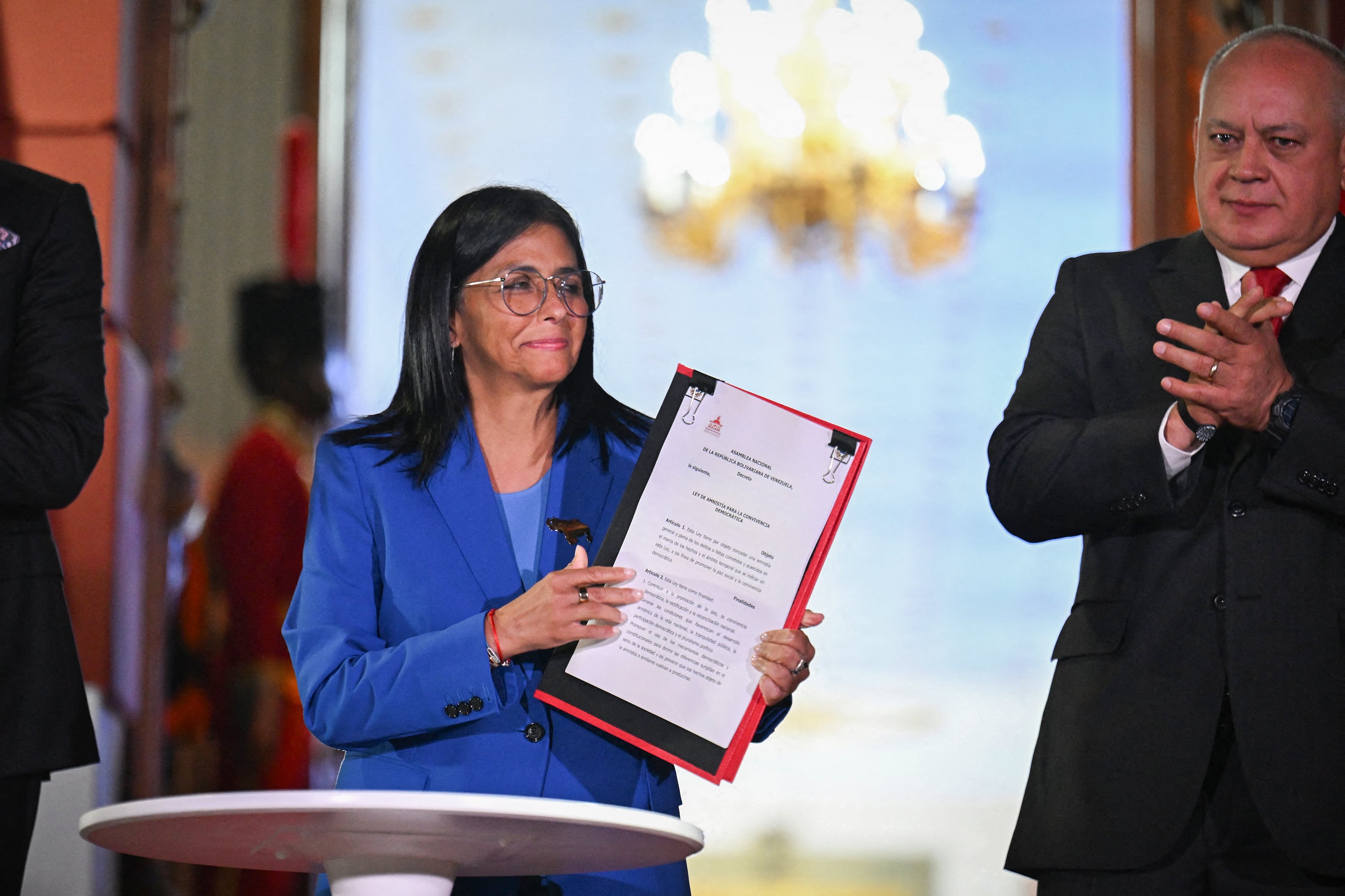 Venezuela's interim president Delcy Rodriguez (C) holds the amnesty law approved by the National Assembly, accompanied by the president of the Assembly Jorge Rodriguez (L, out of frame) and the Minister of Interior, Justice and Peace Diosdado Cabello