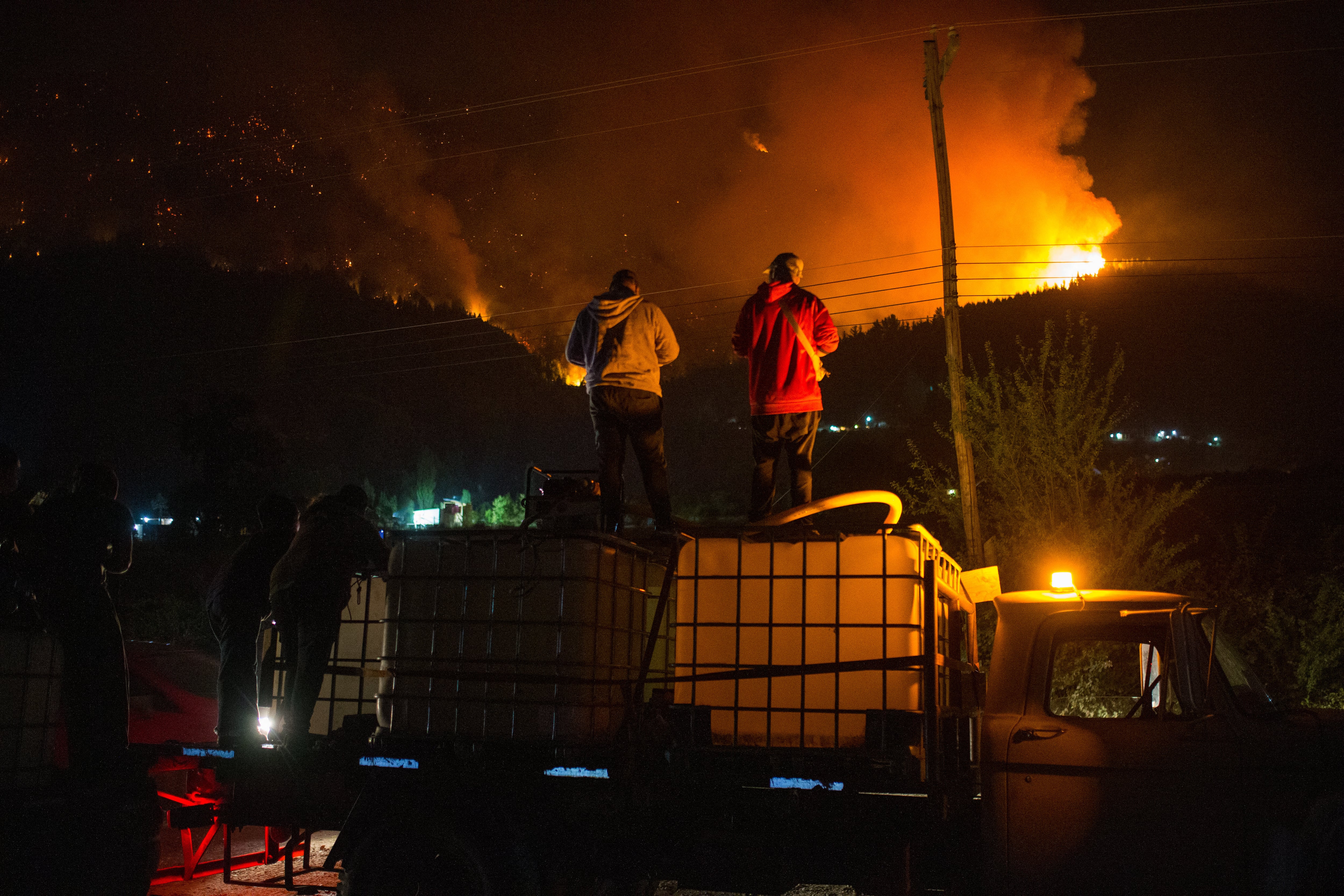 People wait on top of a water truck as a forest fire burns at Mount Pirque at El Hoyo, in the Patagonian region of Chubut province, Argentina on January 7, 2026. Thousands of hectares of forest were devastated by fire on January 6, in Argentine Patagonia, where a red alert is in effect due to extreme conditions, one year after the region experienced its worst wildfires in three decades. (Photo by Martin LEVICOY / AFP)