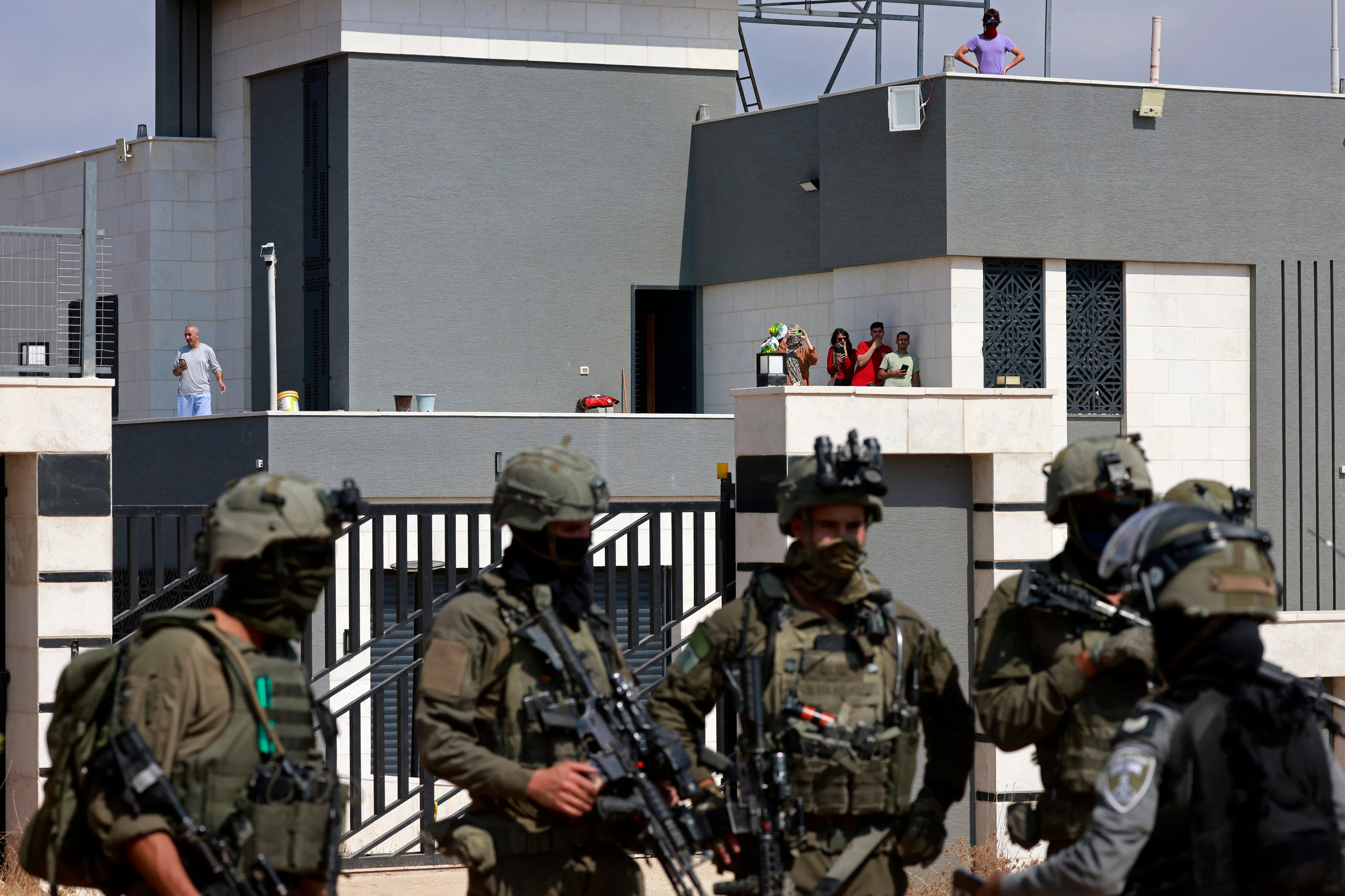 Israeli soldiers stand in front of the entrance of a besieged Palestinian house by Israeli settlers in the village of Qusra, south of Nablus, in the occupied West Bank, on August 14, 2026. Israeli forces on August 13 moved against rogue settlers laying siege to Palestinians amid unusually strong US criticism, even as Israel inaugurated an emblematic settlement elsewhere in the West Bank. Settlers at Qusra near Nablus since August 9 have blockaded Palestinian homes, including one owned by a US citizen, with residents saying they have been cut off from food and other supplies. (Photo by Jaafar ASHTIYEH / AFP)