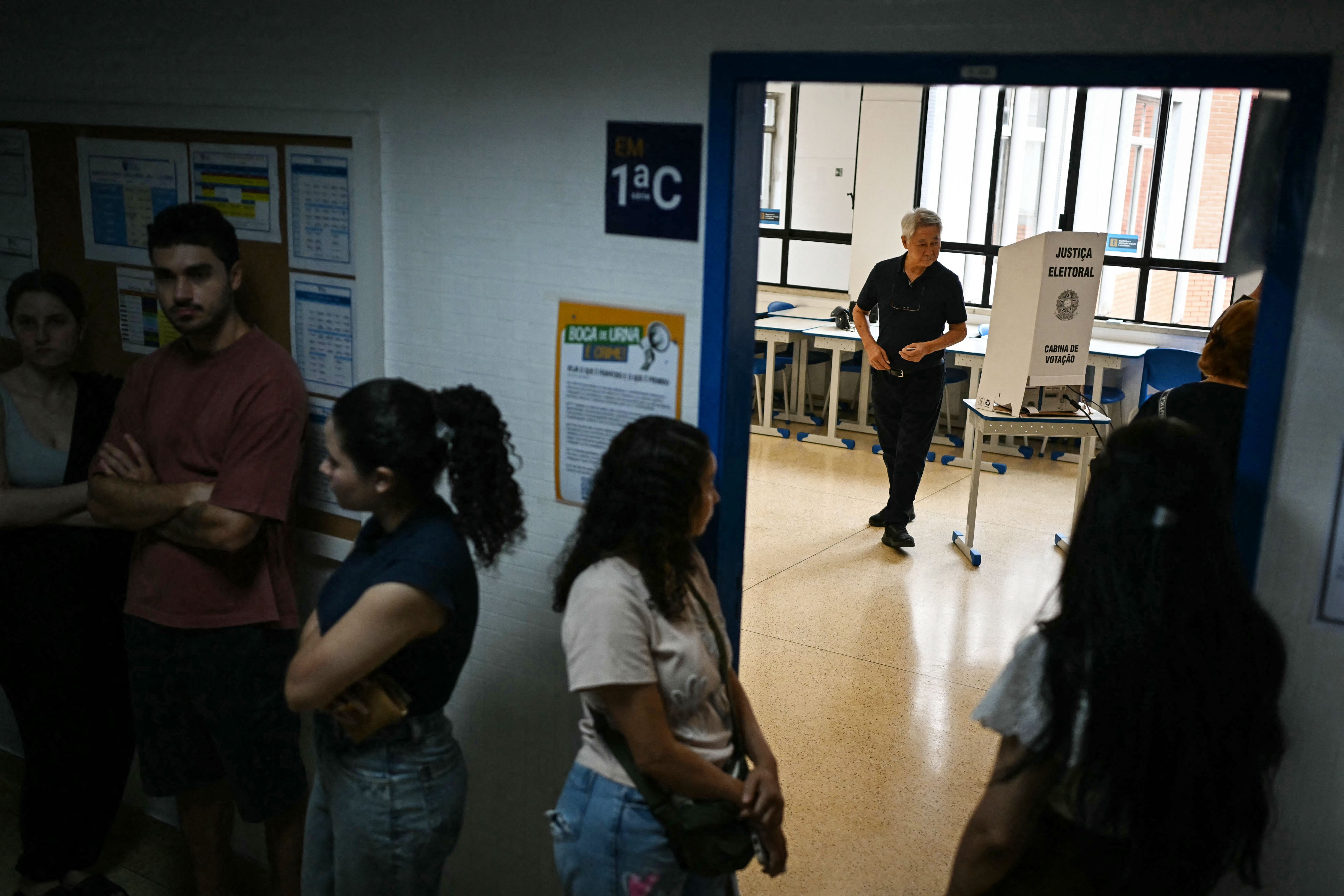 A man is seen after casting his ballot while other people wait to vote in the general election in Sao Paulo, Brazil, on October 4, 2026. Brazilians head to the polls in a highly polarized presidential election between incumbent leftist President Luiz Inacio Lula da Silva -seeking a fourth presidential mandate- and right-wing senator Flavio Bolsonaro, who emerged as the leading figure of the conservative movement following the conviction and imprisonment of his father, former president Jair Bolsonaro. (Photo by Luis ROBAYO / AFP)
