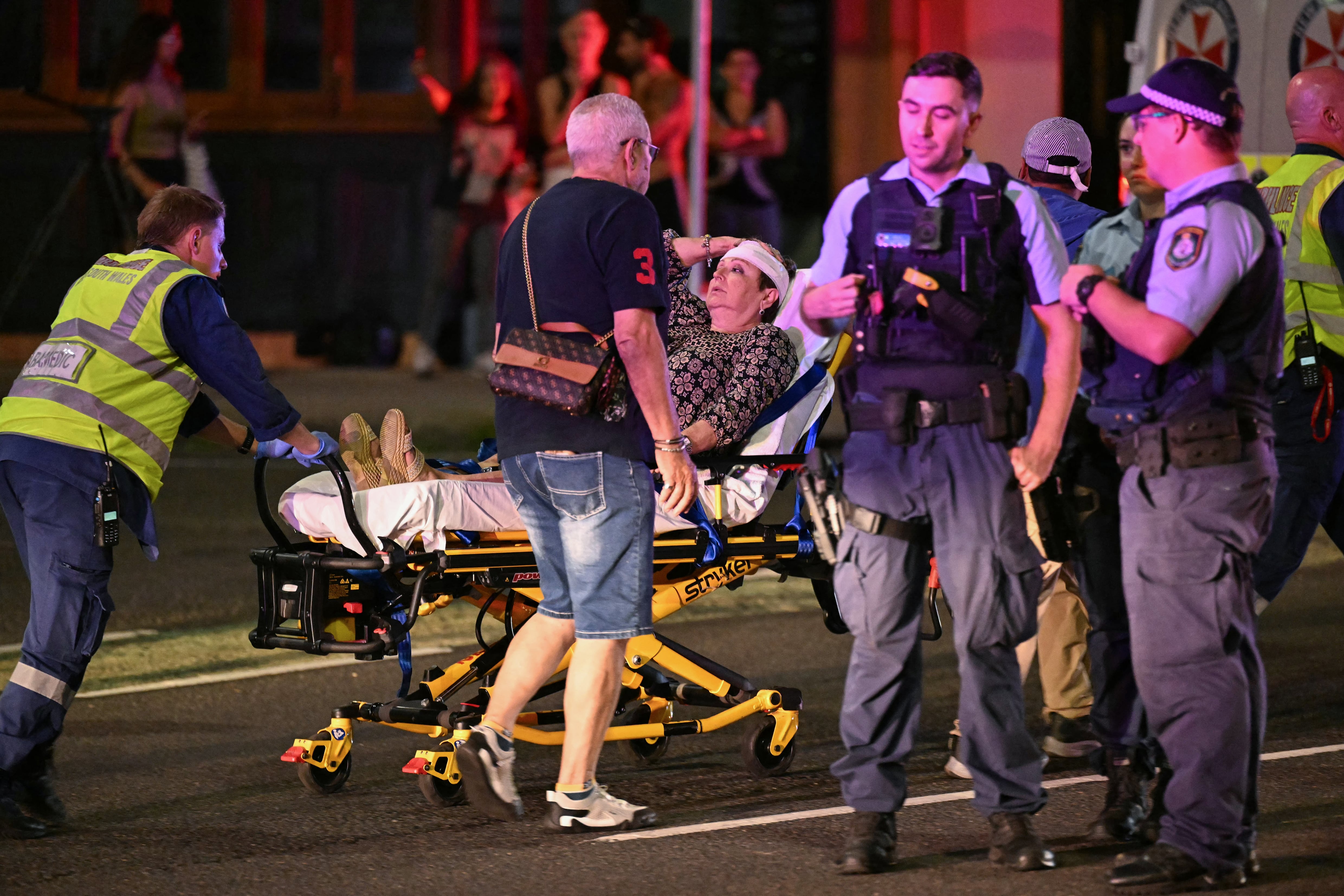 Health workers move a woman on a stretcher to an ambulance after a shooting incident at Bondi Beach in Sydney on December 14, 2025. Australian police said two people were in custody following reports of multiple gunshots on December 14 at Sydney's famed Bondi Beach, urging the public to take shelter. (Photo by Saeed KHAN / AFP)